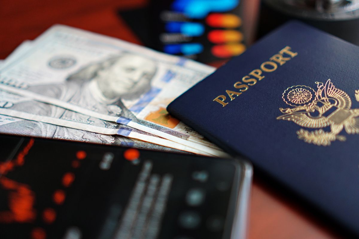 A US passport resting on a fan of hundred-dollar bills beside a smartphone