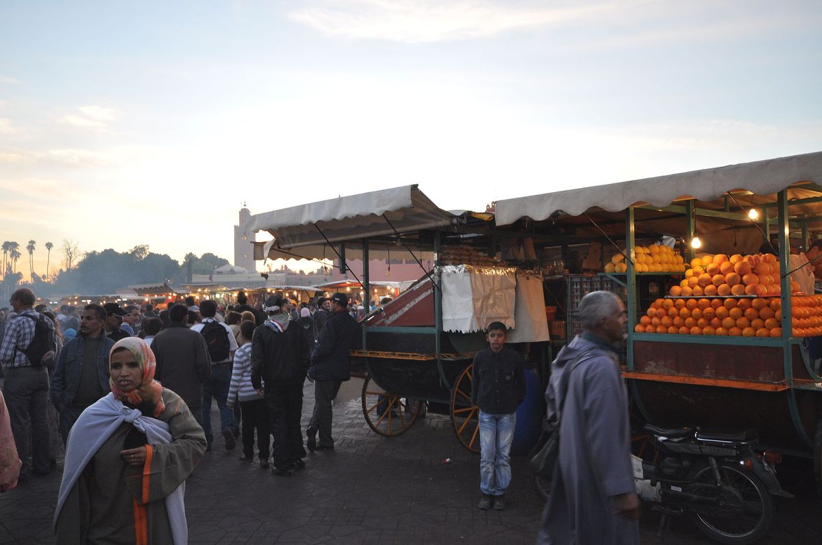 Crowded market square at dusk with orange juice carts and food stalls in Marrakesh